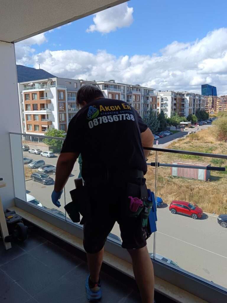 Почистване на прозорци у дома и стъклени повърхности – служител на АКСИ-ЕЛ почиства парапет на тераса